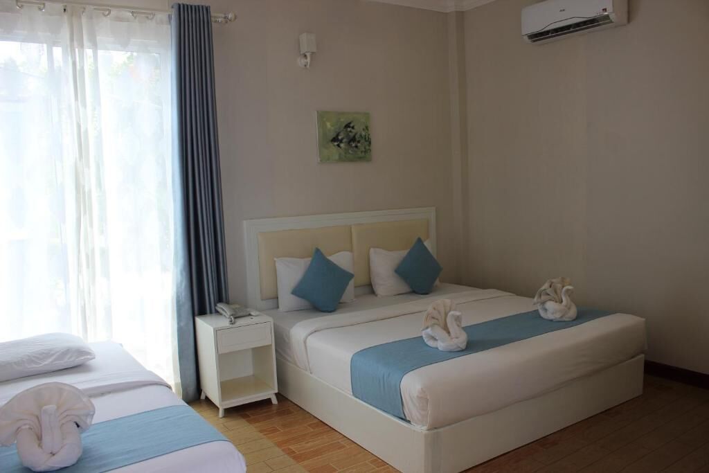 A hotel room with a bed, a nightstand, a wall-mounted air conditioner, and a window with curtains.