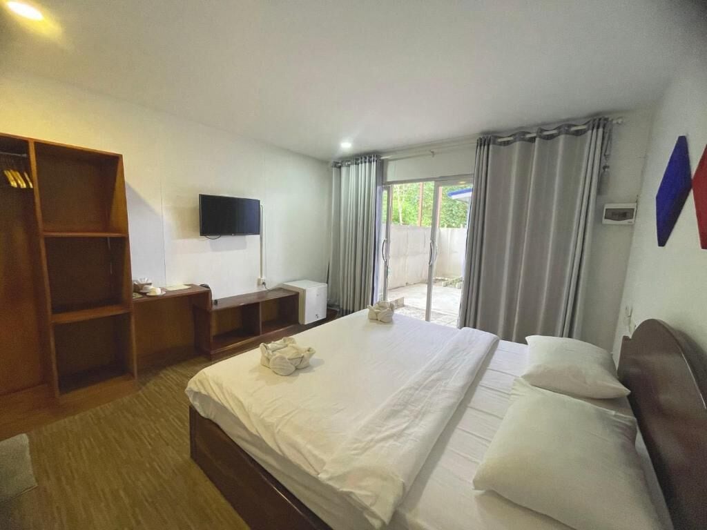 Quarto de hotel com cama, guarda-roupa de madeira, televisão de tela plana e janela com cortinas.