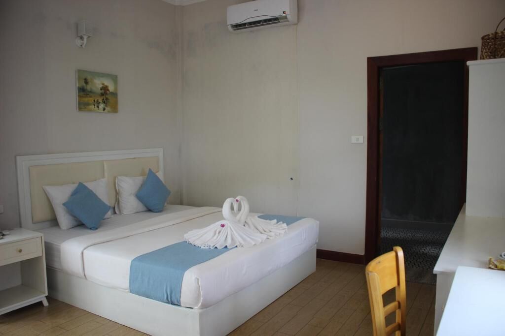 Una habitación de hotel con cama, escritorio, silla, equipo de aire acondicionado y un cuadro en la pared.