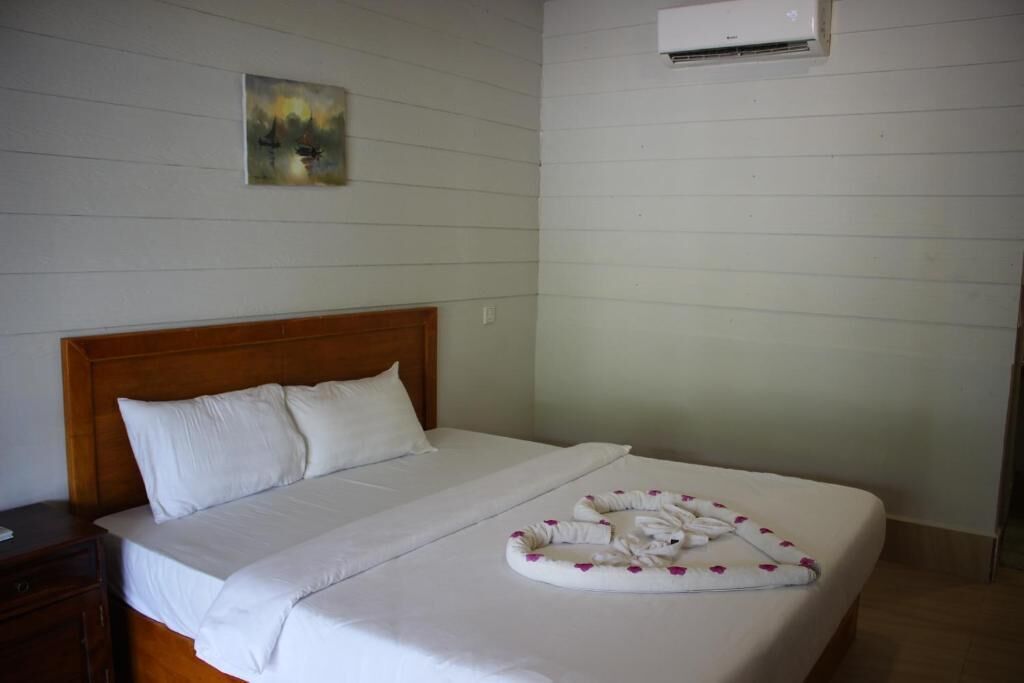 Une chambre d’hôtel avec un lit, une tête de lit, un tableau au mur et un appareil de climatisation.