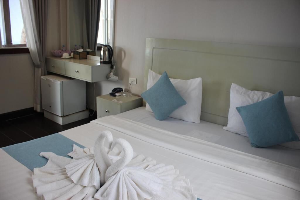 A hotel room with a bed, a bedside table, a nightstand, a mirror, and a window with curtains.