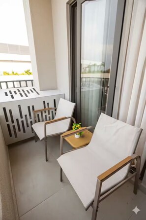 Ein Balkon mit zwei weißen Sitzgelegenheiten und einem Tisch mit einer Pflanze.