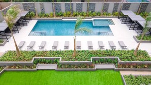 Ein rechteckiger Pool mit mehreren Liegestühlen und einer kleinen Palme.