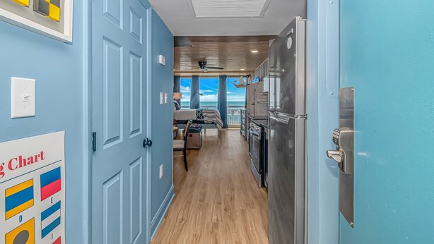 A hallway with a blue door, a kitchen area with a refrigerator, and a dining area with a view. - Yachtsman S503B Studio (Myrtle Beach)