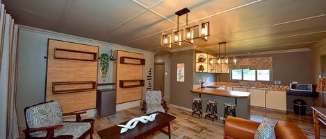 A living room with a sofa, chairs, a coffee table, and a kitchen area with a bar and stools.