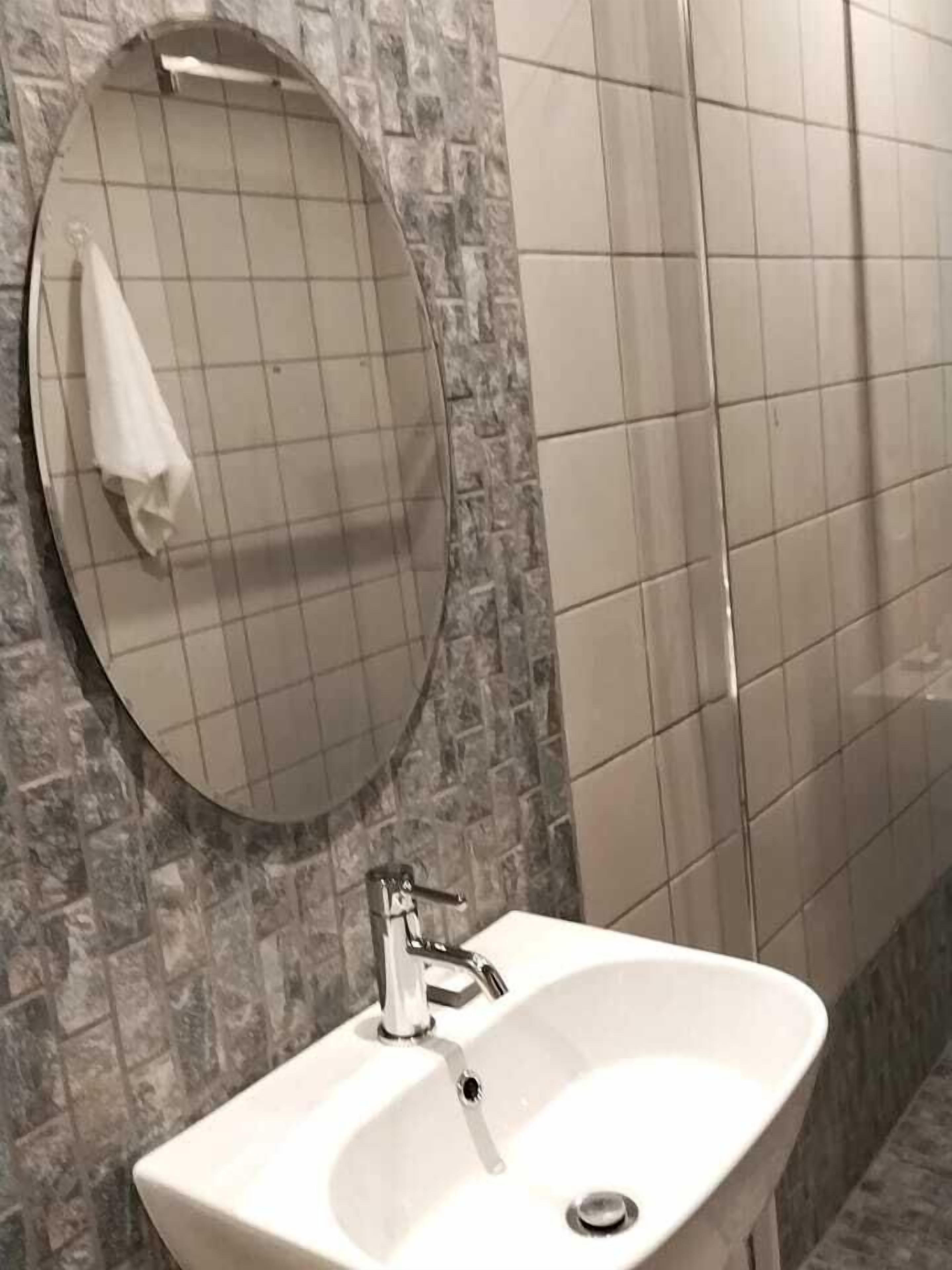 A bathroom with a white sink, a round mirror, and tiled walls.