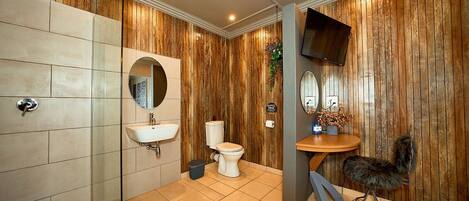 A bathroom with a wooden wall panel, a white toilet, a sink with a mirror, and a television mounted on the wall.