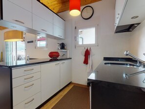 A modern kitchen with white cabinets, a red kettle, a clock, and a window. - Soras Demarmels Appartement/Fewo, Dusche, WC, 2 Schlafräume by Interhome (Savognin)