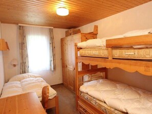 Ein Zimmer mit Etagenbetten, einem Holztisch, einem Schrank und einem Fenster mit Vorhängen.