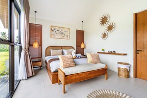 A bedroom with a wooden bed, a bedside table, a hanging light, a wall-mounted artwork, and a view of the outdoors. - 2-bedroom house in peaceful Gianyar with private pool and natural views (Gianyar)