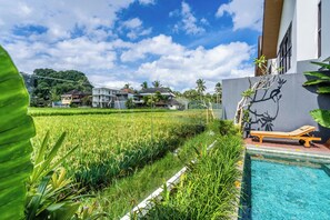 A swimming pool with a lounge chair, a grassy area with a view of houses, and a clear sky. - 2-bedroom house in peaceful Gianyar with private pool and natural views (Gianyar)