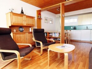 Een kamer met twee zwarte stoelen, een houten kast, een kleine tafel en een kitchenette.