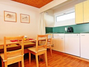 Une petite cuisine avec des chaises en bois, une table à manger, des placards blancs et un plan de travail vert.