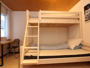 Ein Stockbett mit einer Leiter, einem Schreibtisch und einem Stuhl in einem Raum mit Holzboden und -wänden.