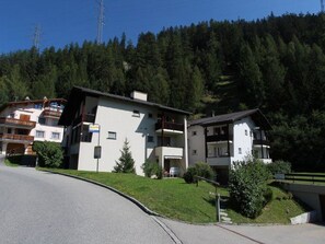 Ein modernes Gebäude mit flachem Dach, einem Balkon und einem kleinen Gartenbereich.
