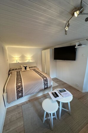 A bedroom with a bed, bedside lamps, a TV, a desk, and a chair. - Jonnys Paradisli Appartement/Fewo, Dusche und Bad, WC, 1 Schlafraum by Interhome (Cunter)