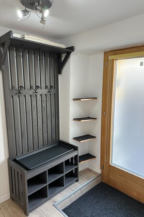 Eine Hausecke mit einer dunklen Holzbank, einem an der Wand befestigten Regal und einer Tür.