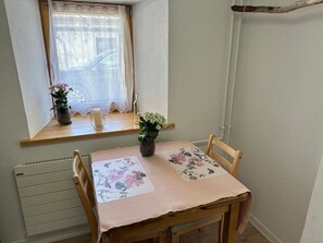 A dining area with a table set for two, a window with a curtain, and a radiator below. - Jonnys Paradisli Appartement/Fewo, Dusche und Bad, WC, 1 Schlafraum by Interhome (Cunter)
