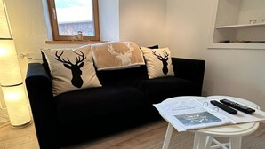 A cozy living room with a black sofa, a white coffee table, and a window with a view. - Jonnys Paradisli Appartement/Fewo, Dusche und Bad, WC, 1 Schlafraum by Interhome (Cunter)