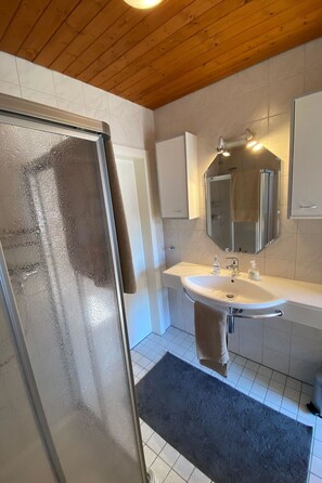 Een badkamer met een douchecabine van glas, een wit wastafelmeubel, een spiegel en een handdoekhouder.