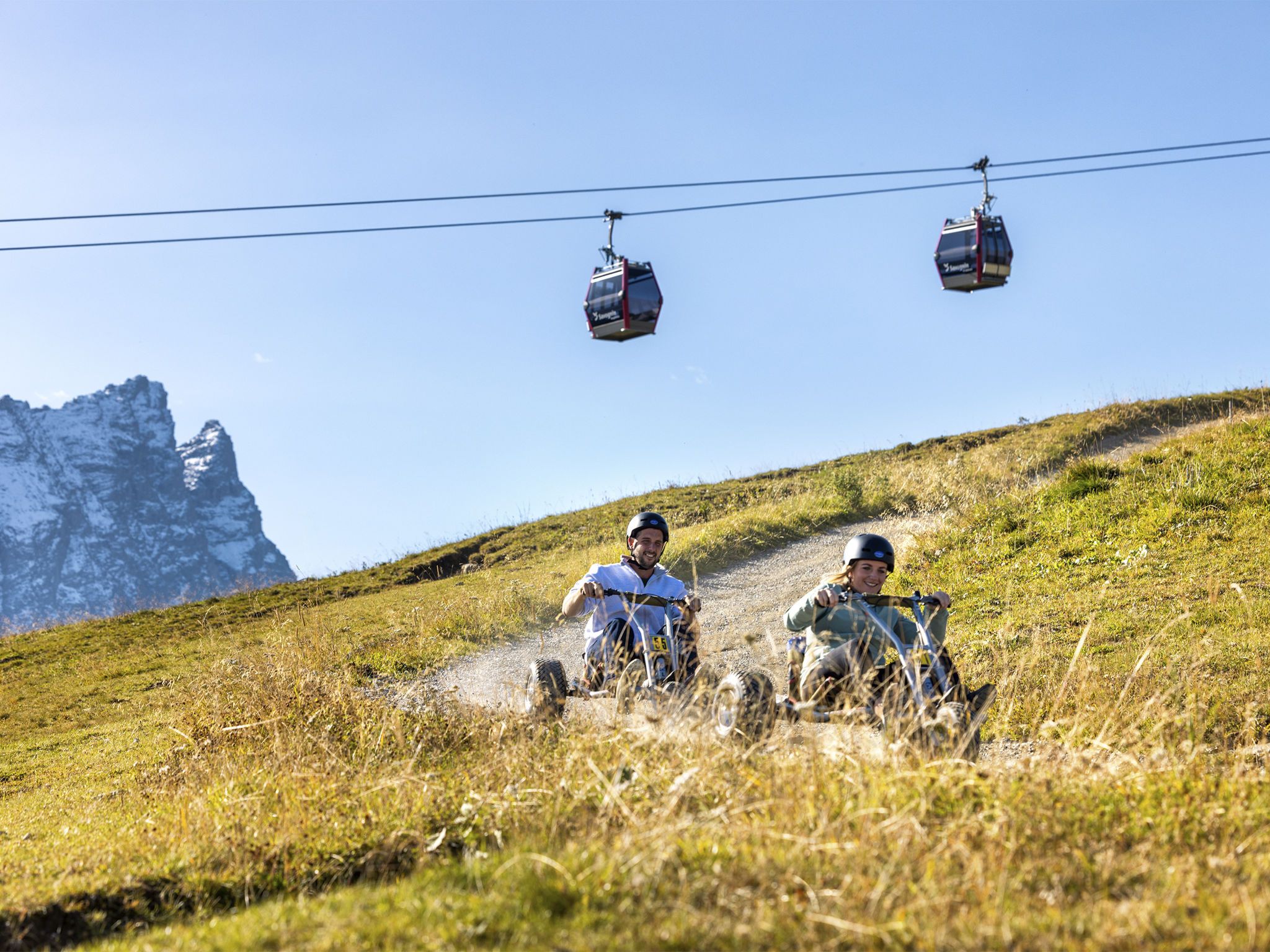 Berglandschap met een skifaciliteit en twee personen op een onverharde weg.