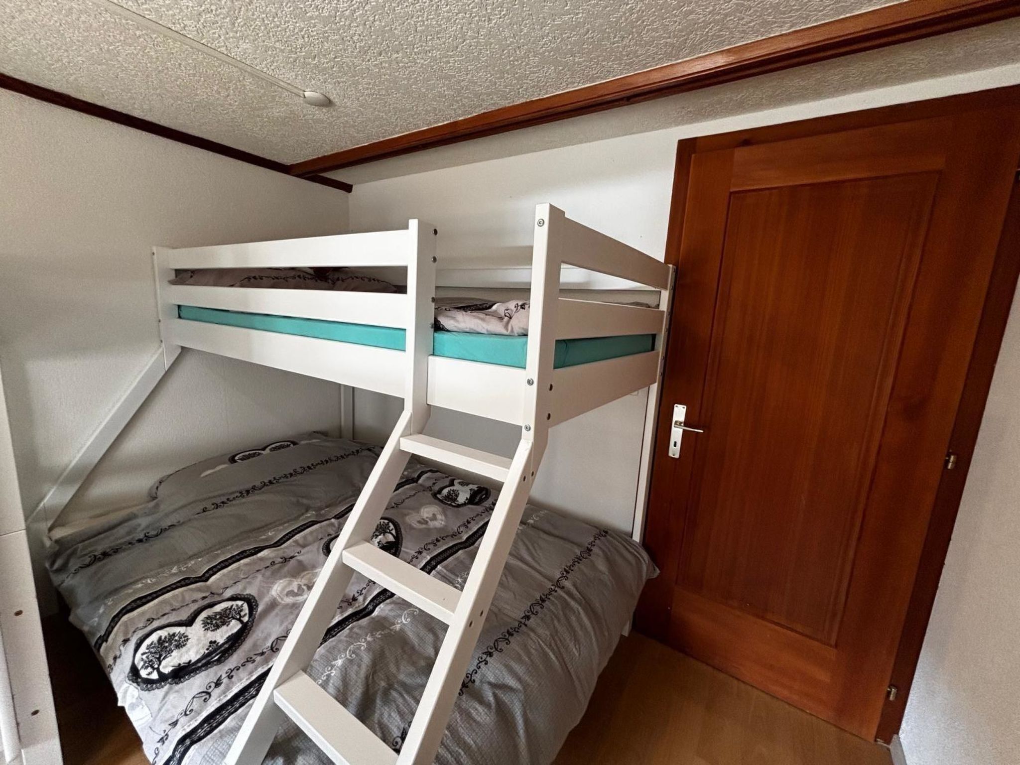 Een stapelbed met een ladder, een deur en een bedovertrek met een patroon.