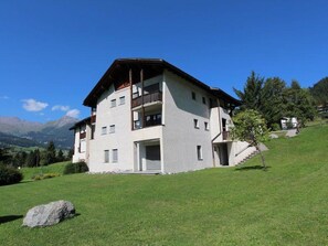 Ein mehrstöckiges Gebäude mit flachem Dach, einem Balkon im zweiten Stock und einer Treppe, die zum Eingang führt.