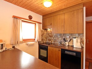 A compact kitchen with wooden cabinets, a built-in stove, a sink, and a coffee maker. - Soras 10 A Appartement/Fewo, Bad, WC, 2 Schlafräume 3 Zimmerwohnung - 4 Betten by Interhome (Savognin)