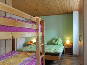 Habitación con literas, una cama individual con almohadas y dos mesitas de noche con lámparas.
