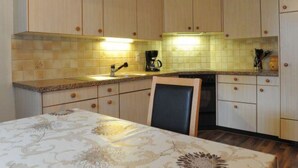 A kitchen with wooden cabinets, a tiled backsplash, a coffee maker, and a table with a patterned tablecloth. - Ferienwohnung Hof Collet Appartement/Fewo, Dusche oder Bad, WC, 1 Schlafraum by Interhome (Cunter)