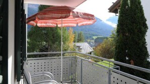 A balcony with a metal railing, a wooden bench, and a red umbrella. - Ferienwohnung Hof Collet Appartement/Fewo, Dusche oder Bad, WC, 1 Schlafraum by Interhome (Cunter)