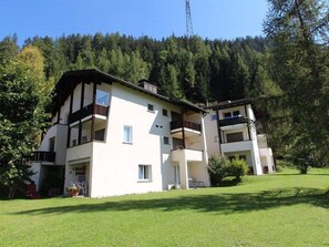 Ein zweistöckiges Gebäude mit Balkonen, einer grünen Rasenfläche und einem bewaldeten Hügel im Hintergrund.
