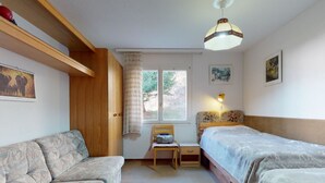 A bedroom with a sofa, two single beds, a chair, a desk, and a window. - Soras Zerbe/Hirth Appartement/Fewo, Bad, WC, 1 Schlafraum by Interhome (Savognin)