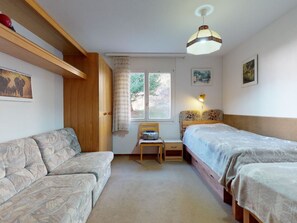 Ein Schlafzimmer mit einer Couch, zwei Einzelbetten, einem Sessel, einem Schreibtisch und einem Fenster.