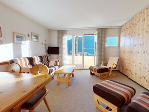 Ein Wohnzimmer mit einer Couch, einem Holztisch, einem Fernseher und Blick durch Glastüren.