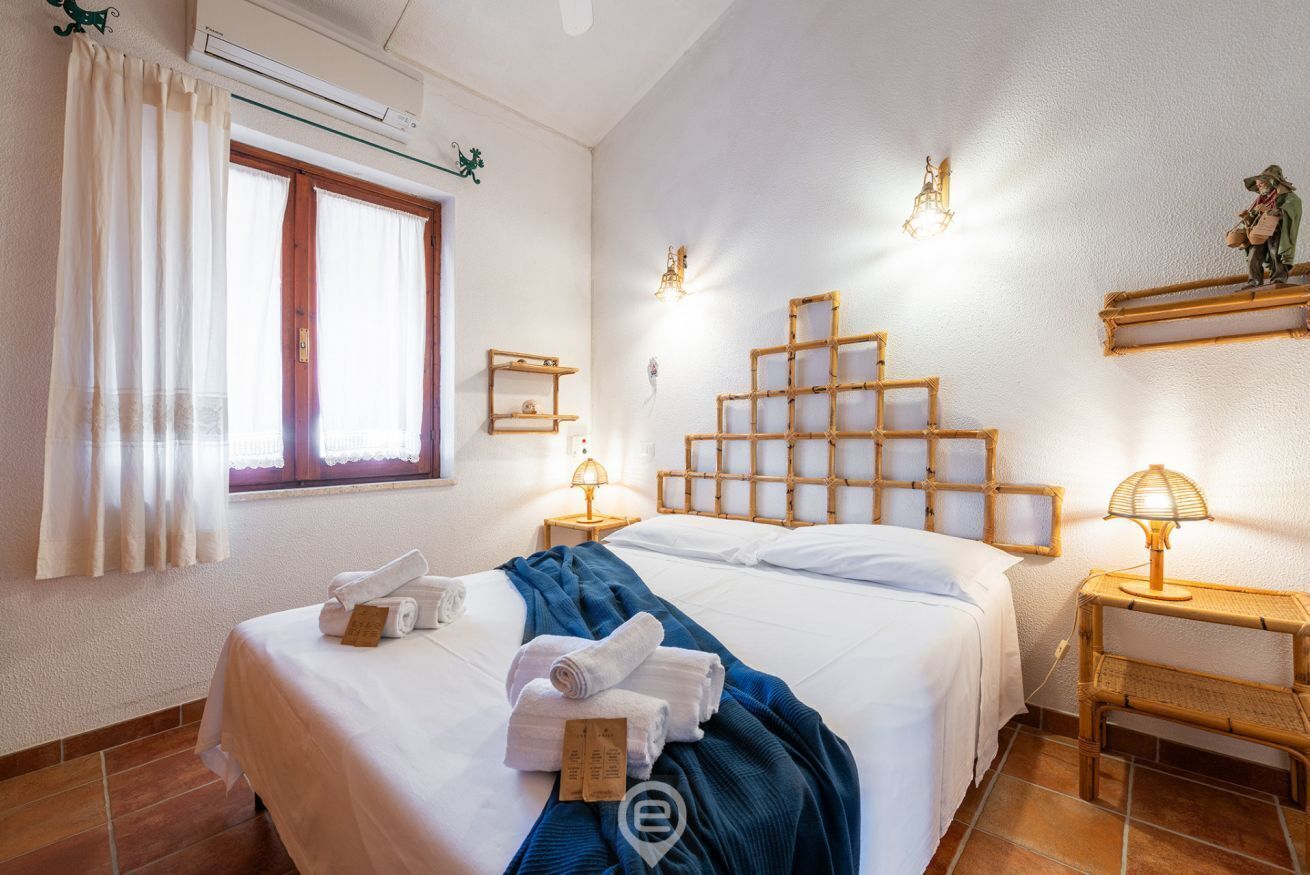 A hotel room with a bed, two bedside tables, a window with curtains, and wall-mounted lights.
