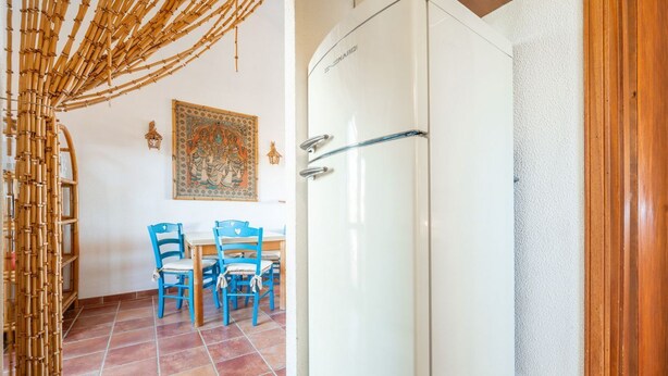 Una stanza con un frigorifero bianco, un tavolo da pranzo con sedie blu e un decoro a parete.