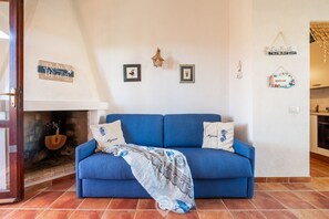 A living room with a blue sofa, a patterned throw blanket, and a fireplace. - Estay - Myricae -Una terrazza a due passi dal mare (Muravera)