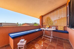 Ein Balkon mit einer blauen Sitzbank, einem kleinen Tisch und einem weißen Laternenleuchter.
