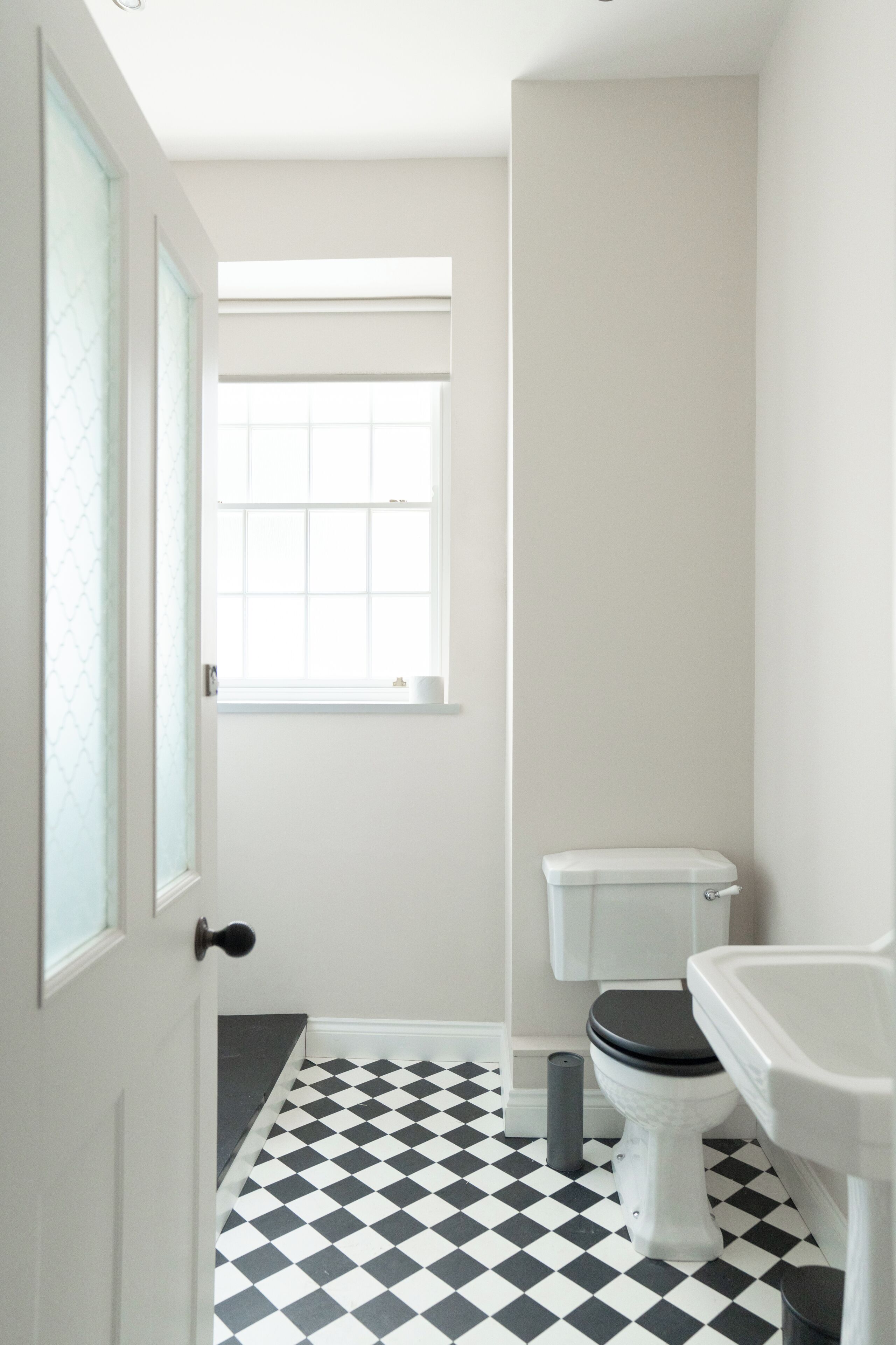 A small, narrow bathroom with a black and white checkered floor, a toilet, a sink, and a window with a grid pattern.