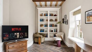 A cozy living room with a wooden TV stand, a bookshelf, and a window with a view.