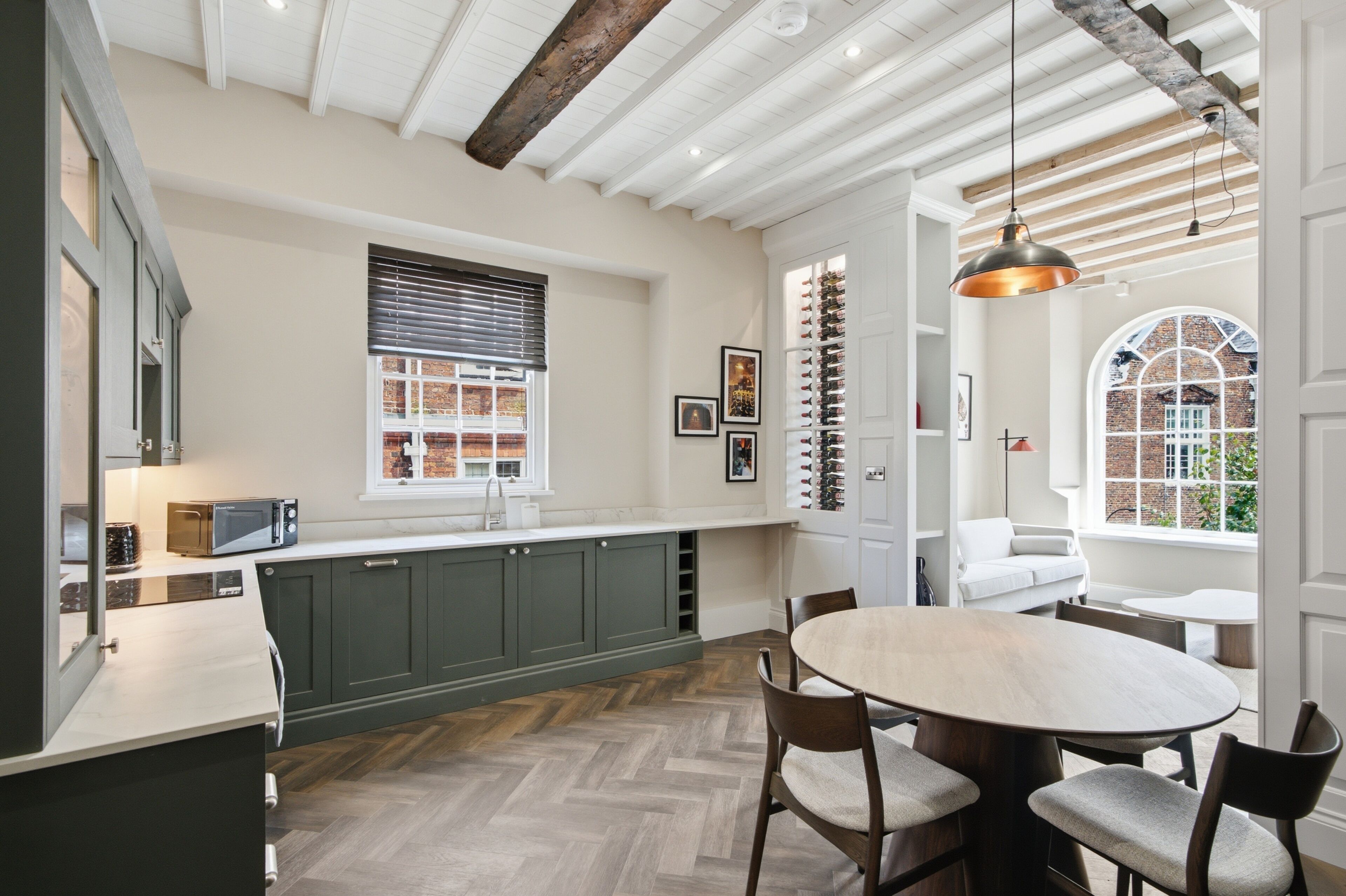 A modern kitchen with dark cabinets, a herringbone floor, and a dining area with a round table and chairs.