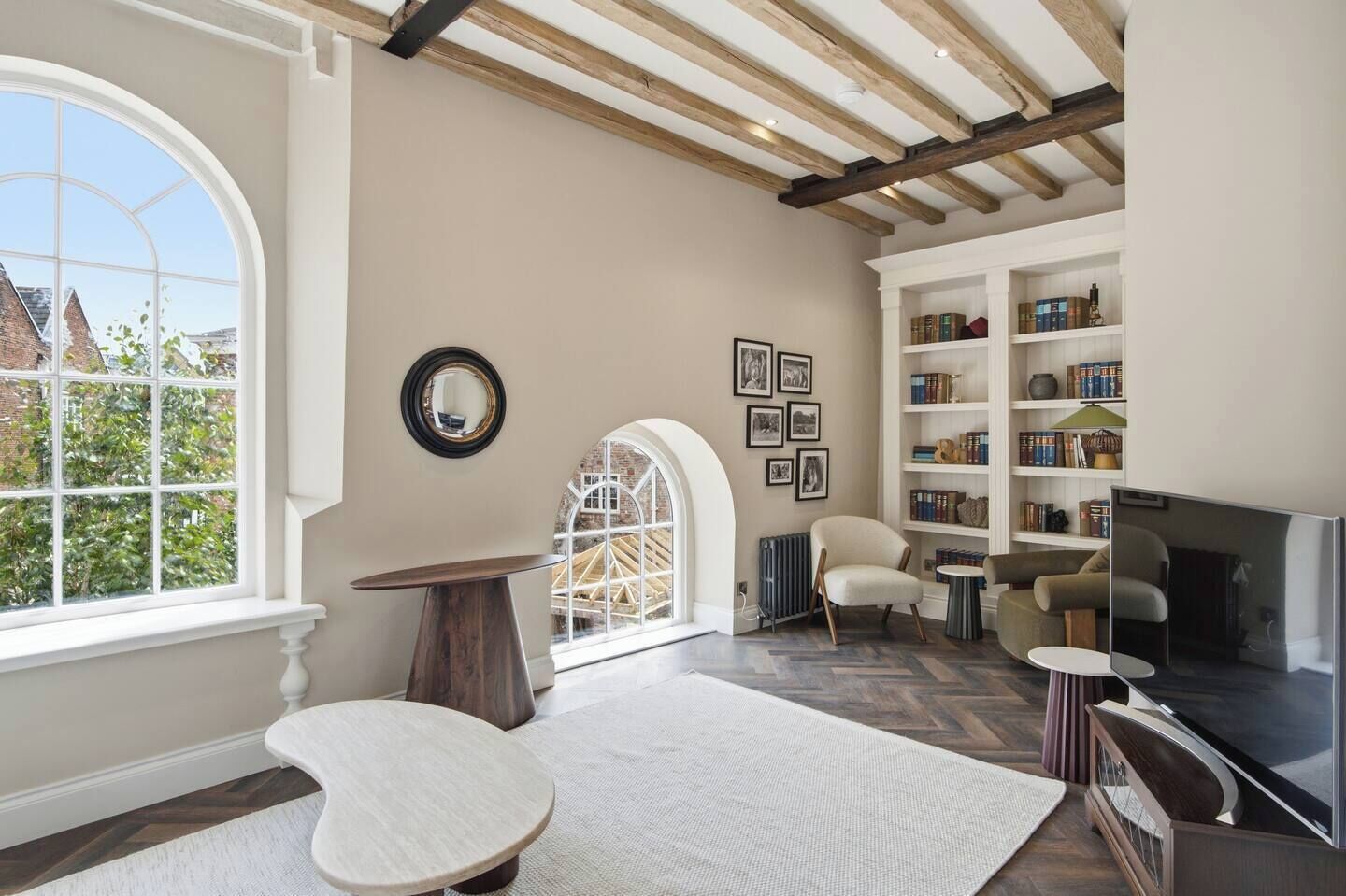A spacious living room with a large window, a fireplace, a bookshelf, and a television.