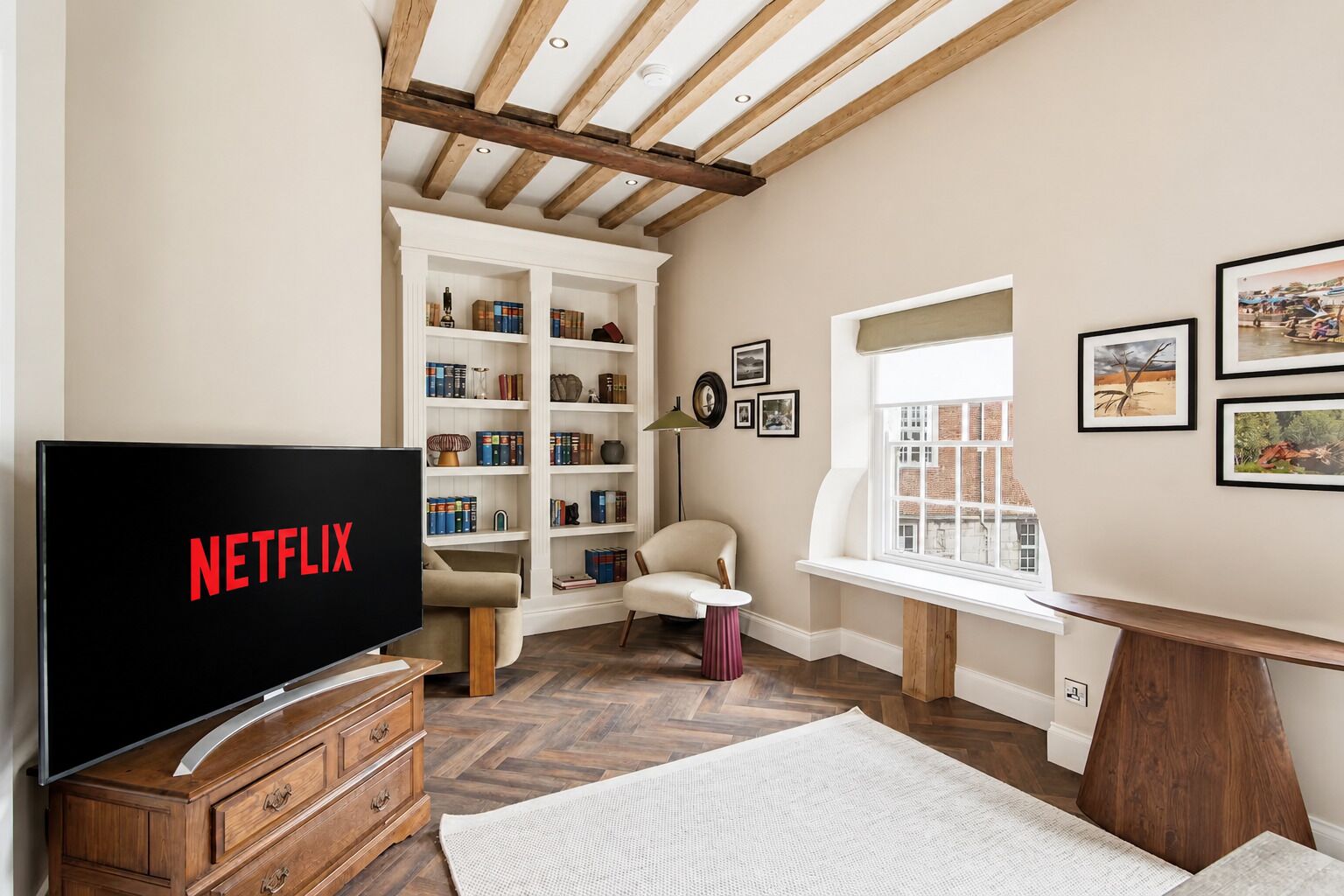 A room with a television displaying 'NETFLIX,' a bookshelf, a window with a view, and a chair.