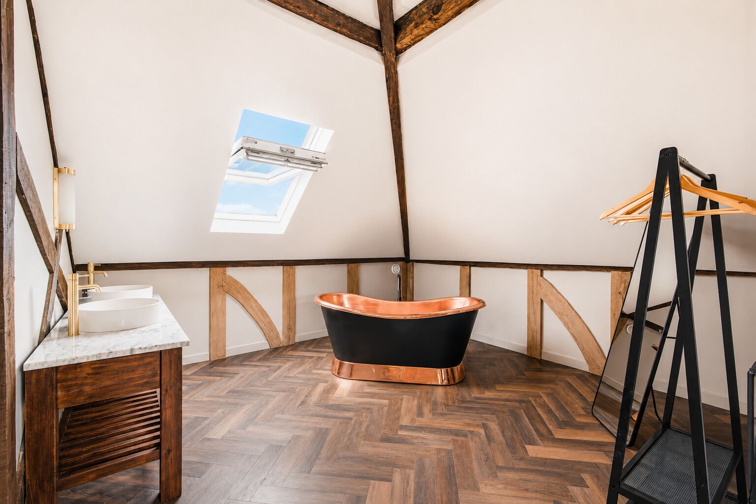 A room with a wooden floor, a black bathtub, a wooden bench, and a skylight.