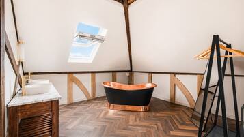 A room with a wooden floor, a black bathtub, a wooden bench, and a skylight.