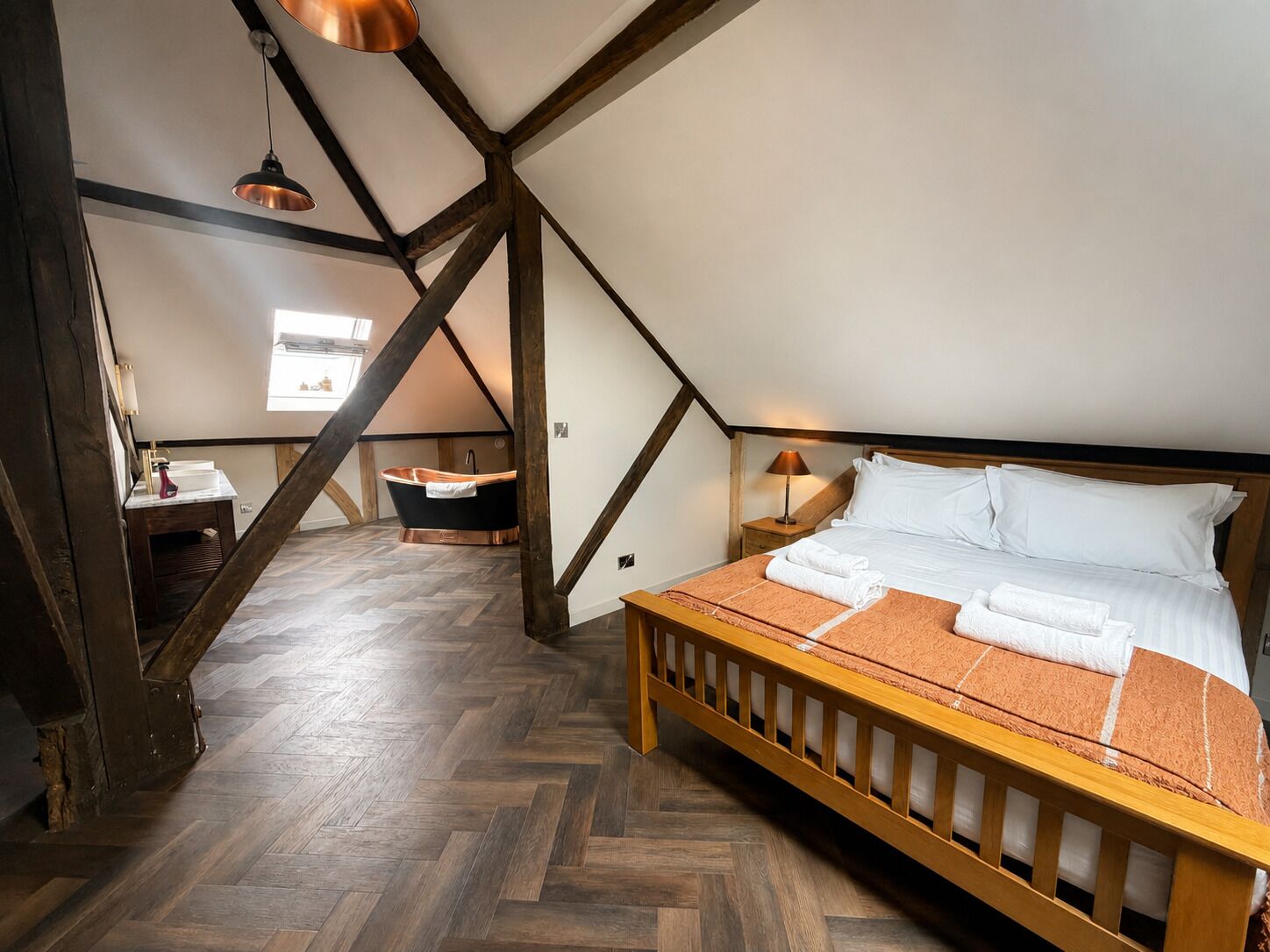 A bedroom with a wooden bed, a herringbone floor, a window, and a bathtub.