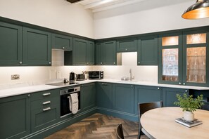 A kitchen with dark green cabinets, a white countertop, a built-in microwave, and a window with a view of a building. - Preachers Yard (York)