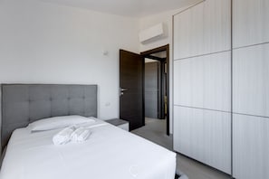 A modern hotel room with a large bed, a wardrobe, and an air conditioning unit. - Mandarin Apartment 5 (Tortolì)