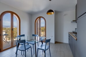 A dining area with a glass table and chairs, large arched windows, and a view of the outdoors. - Mandarin Apartment 5 (Tortolì)
